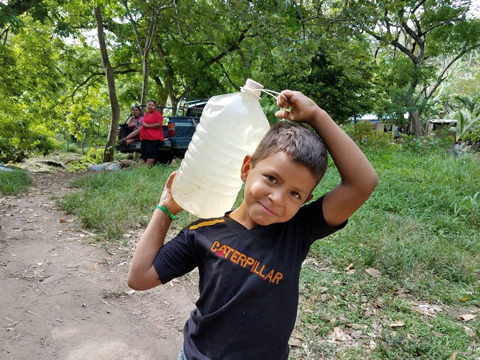 Smiling boy carrying a jug of dirty water in Colonia Alden Webster